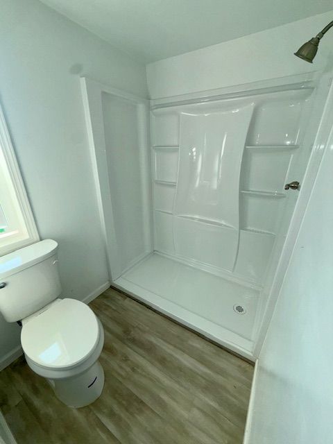 White bathroom with toilet, shower stall, and light wood-look flooring.