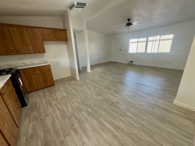 Empty interior, kitchen with wood cabinets, light wood flooring, and a large window.