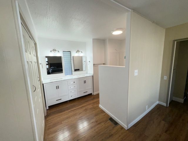 Bathroom with white vanity, mirrors, and wood-look flooring. Partially visible door and beige wall.