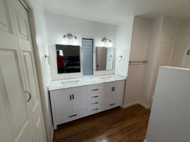 White double vanity with two mirrors and lighting in a bathroom; wood floor.