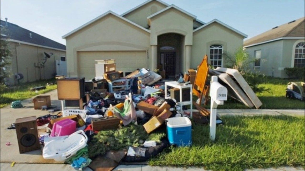 Pile of discarded items, furniture, and trash in front of a house.
