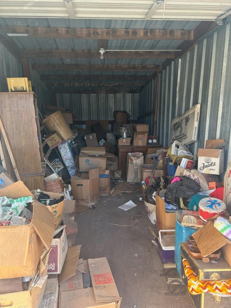 Interior of a storage unit filled with boxes and various items. Dusty, cluttered.