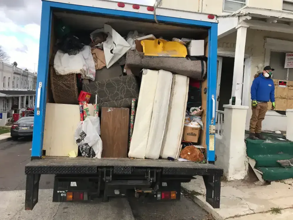 Truck bed overflowing with furniture and boxes; a person in a mask stands on a porch.