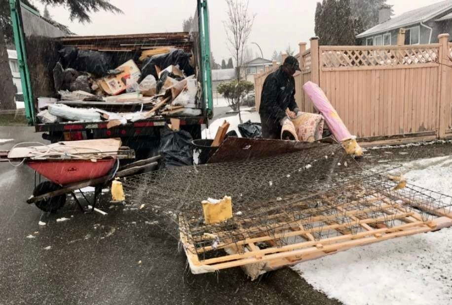 Garbage truck being loaded with debris; worker in dark clothing on snowy street.