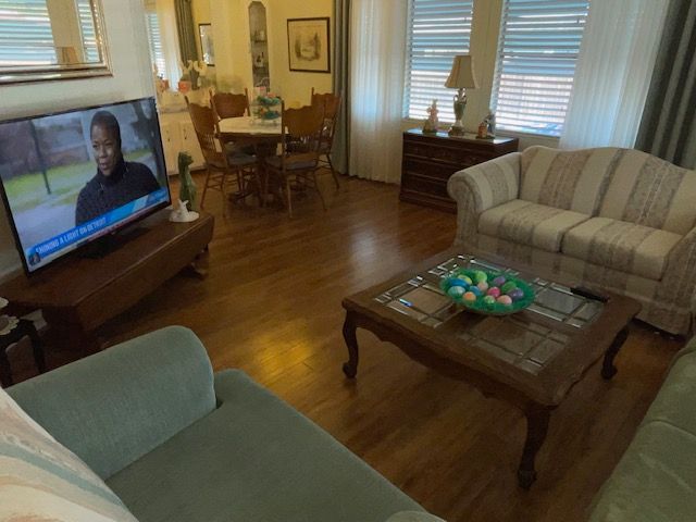 Living room with TV, couch, and dining area. Wooden floors, a coffee table with an Easter egg display.
