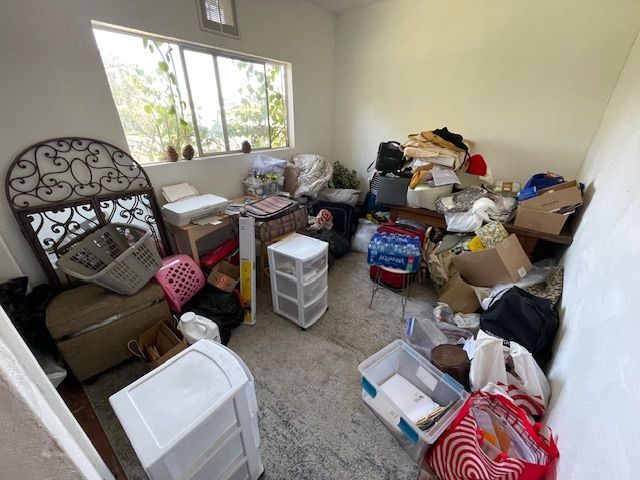 A cluttered room with various items, including boxes and bags, overflowing near a window and wall.