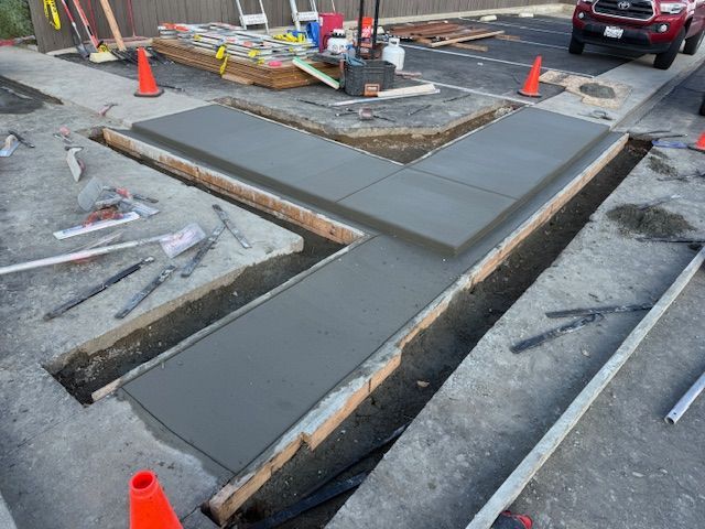 Freshly poured concrete sidewalk section in a construction site, with orange safety cones nearby.