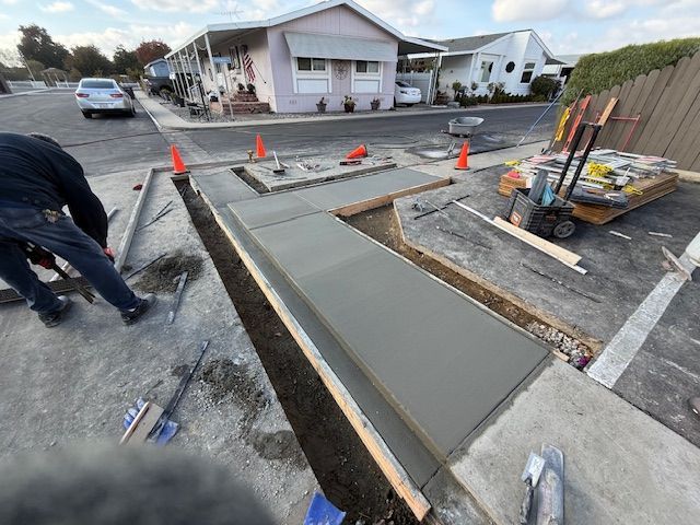 Concrete sidewalk construction. A worker is smoothing wet concrete next to orange cones and houses.