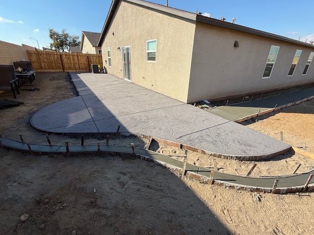 Concrete patio under construction with freshly poured edges, next to a beige house, sunny day.