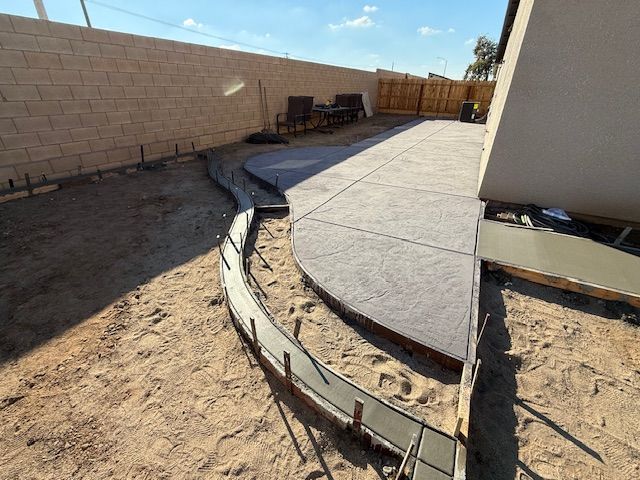 Concrete work in progress in a yard. Gray concrete patio with a curved walkway bordered by rebar.