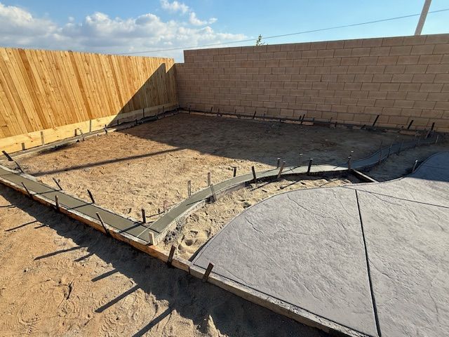 A backyard with concrete forms and stamped patio, with sand and wooden fence.