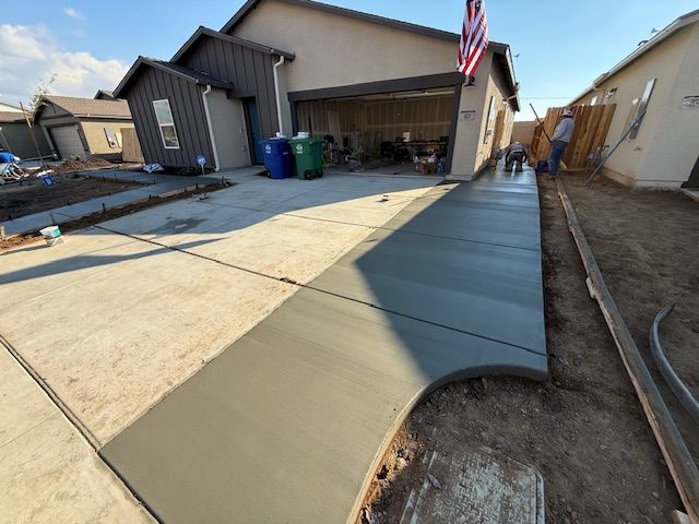 Freshly poured concrete sidewalk and driveway in front of a house, with workers in the background.