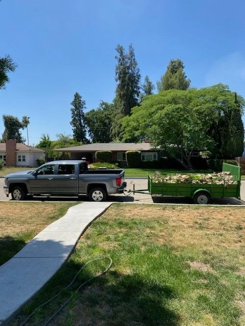 Gray truck towing a green trailer filled with debris parked on a residential street.