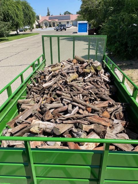Green trailer filled with a pile of firewood.