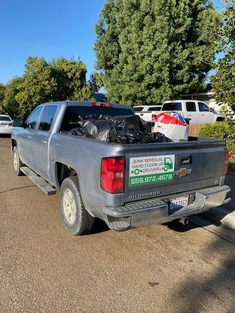 Gray pickup truck with trash bags in the bed, parked on a street. Green and white business sign on the tailgate.