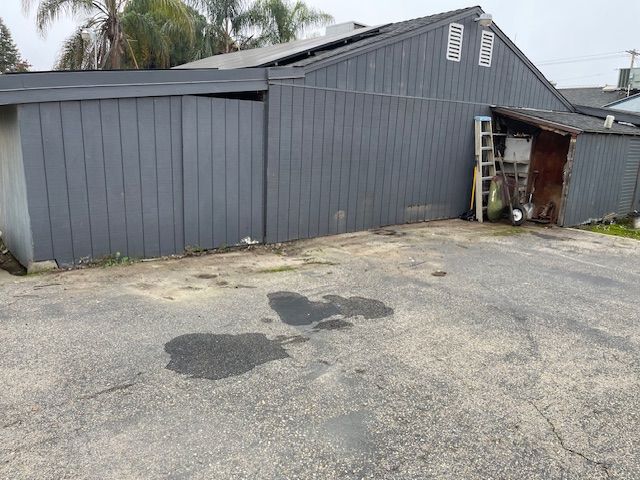 Grey building with asphalt driveway, wet spots.