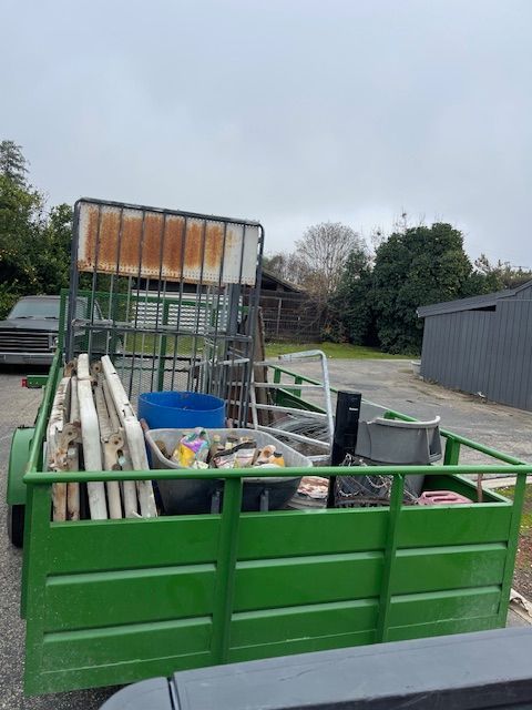 Green trailer filled with metal and debris in an outdoor setting on a cloudy day.