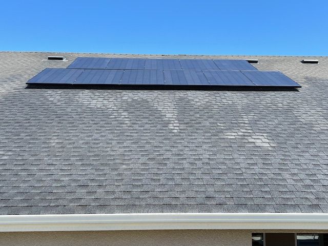 Solar panels installed on a gray shingled roof under a clear blue sky.