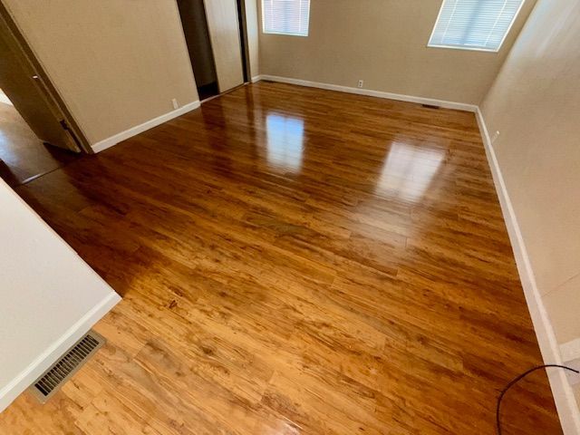 Wooden floor in a room, with sunlight reflecting off its shiny surface. White trim and beige walls.