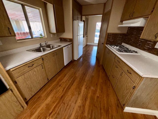 A kitchen with wood cabinets, white countertops, and wood-look flooring. A window, sink, and refrigerator are visible.