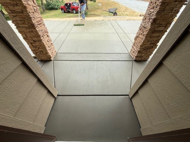 Newly poured concrete driveway with decorative pillars; person smoothing the surface.
