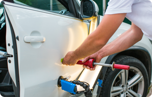 A man is repairing a car door with a hammer.