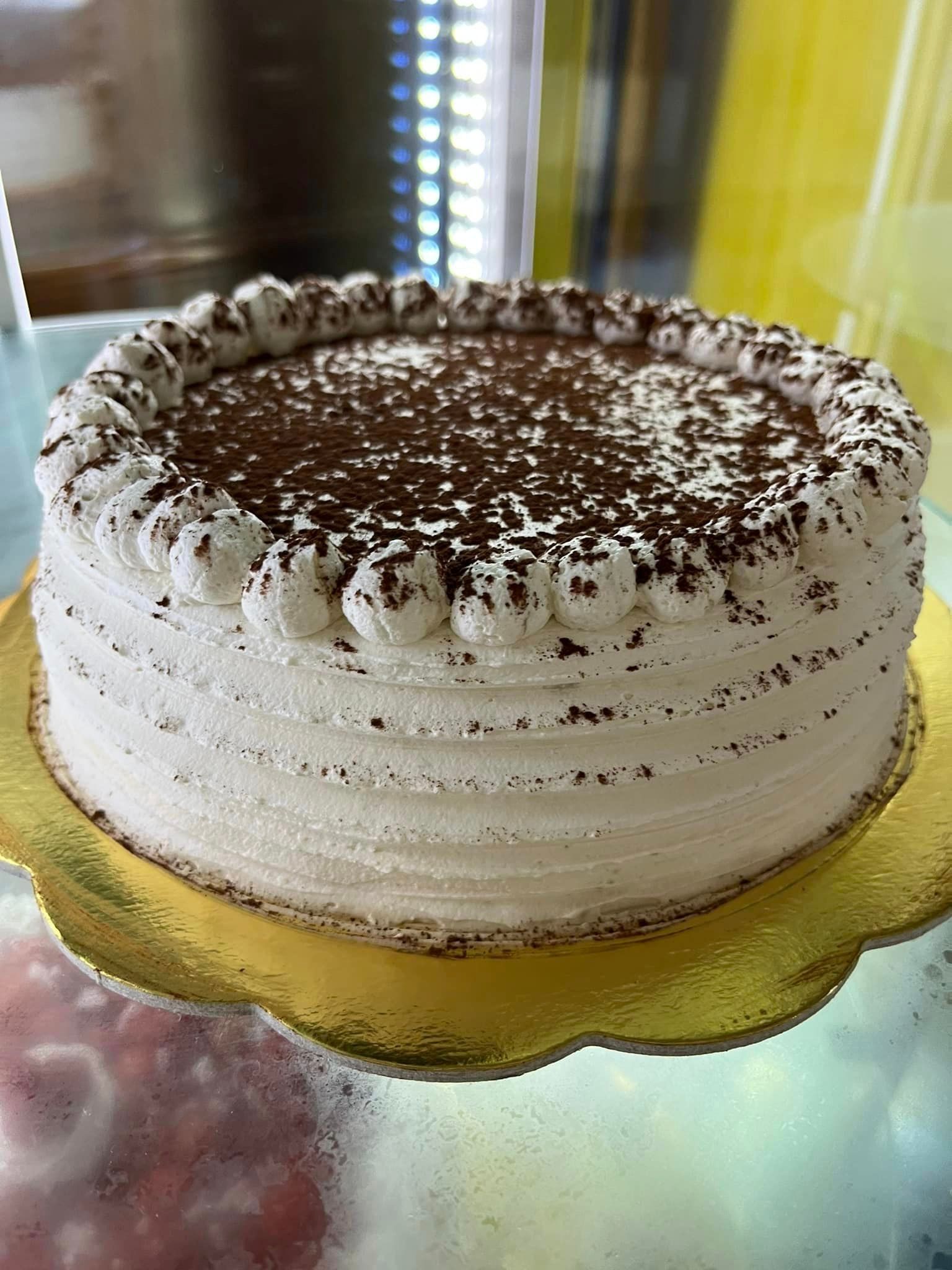 una torta bianca con granelli di cioccolato in cima è seduta su un piatto d'oro.