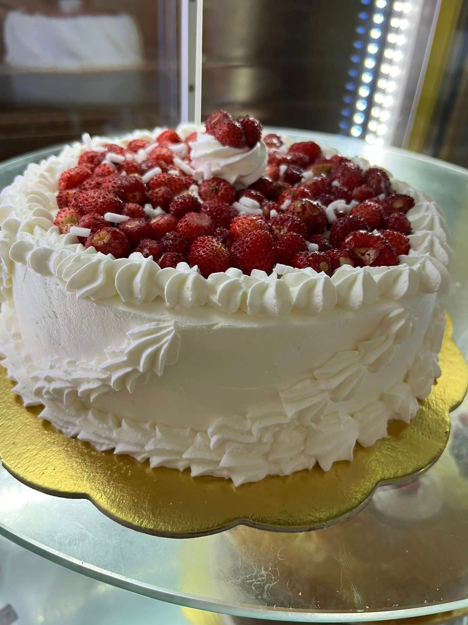su una lastra di vetro c'è una torta con panna montata e fragole sopra.