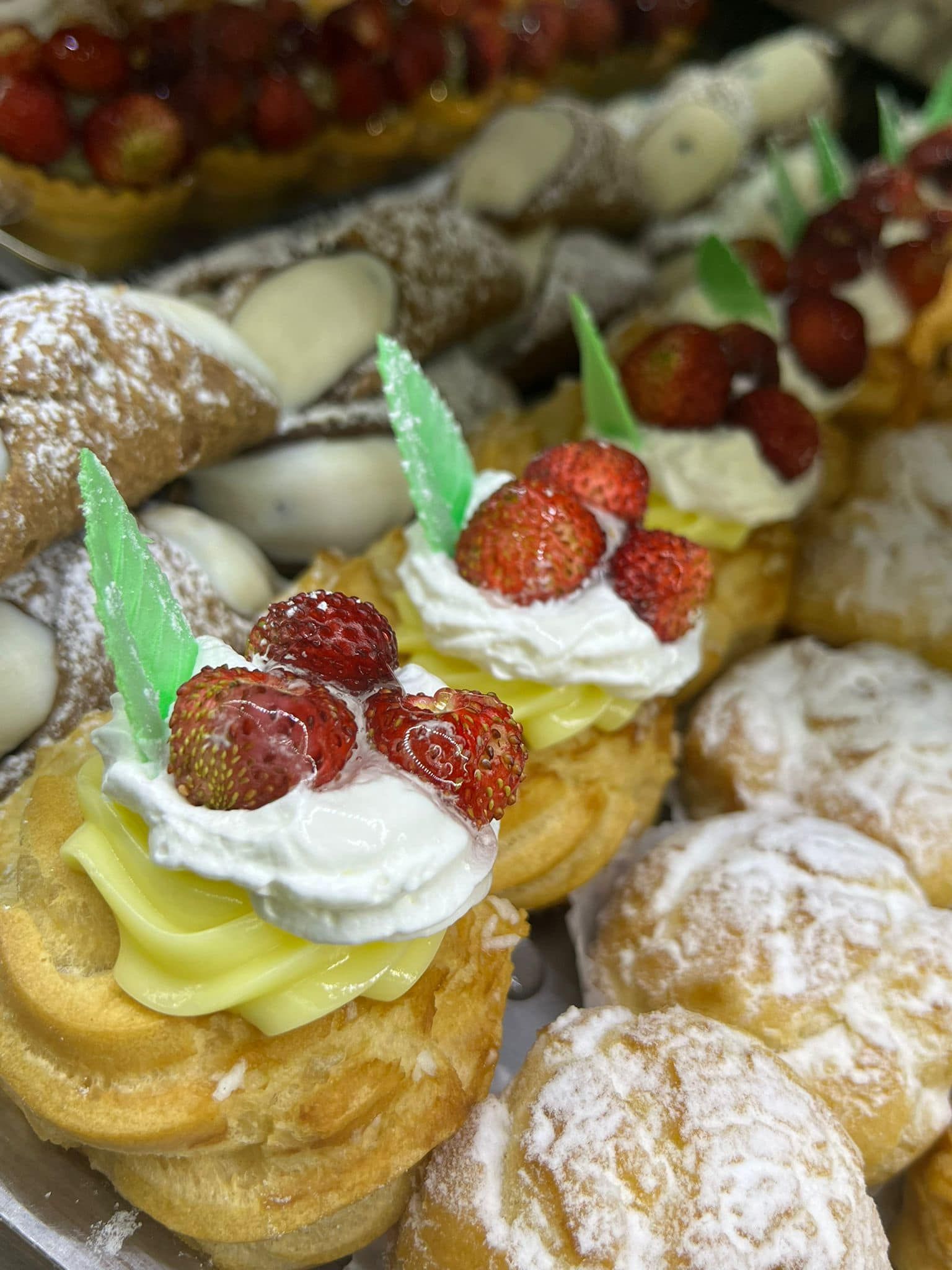 una varietà di pasticcini con panna montata e fragole in cima.