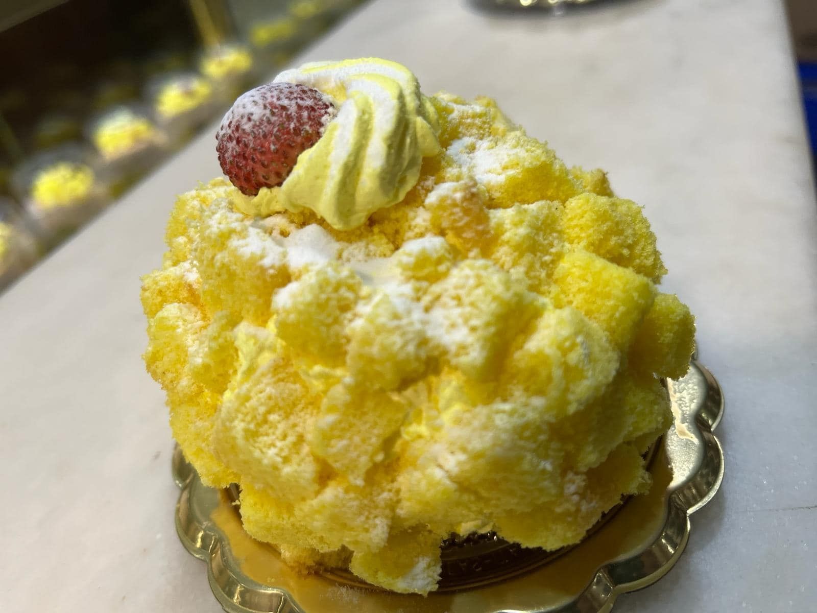 un primo piano di una torta gialla con panna montata e una fragola sopra.