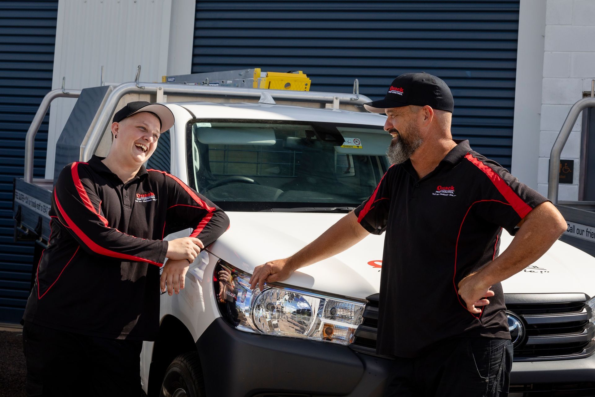 Two People in Work Uniforms Leaning on a White Truck — Quack Pest Control in Howard Springs, NT