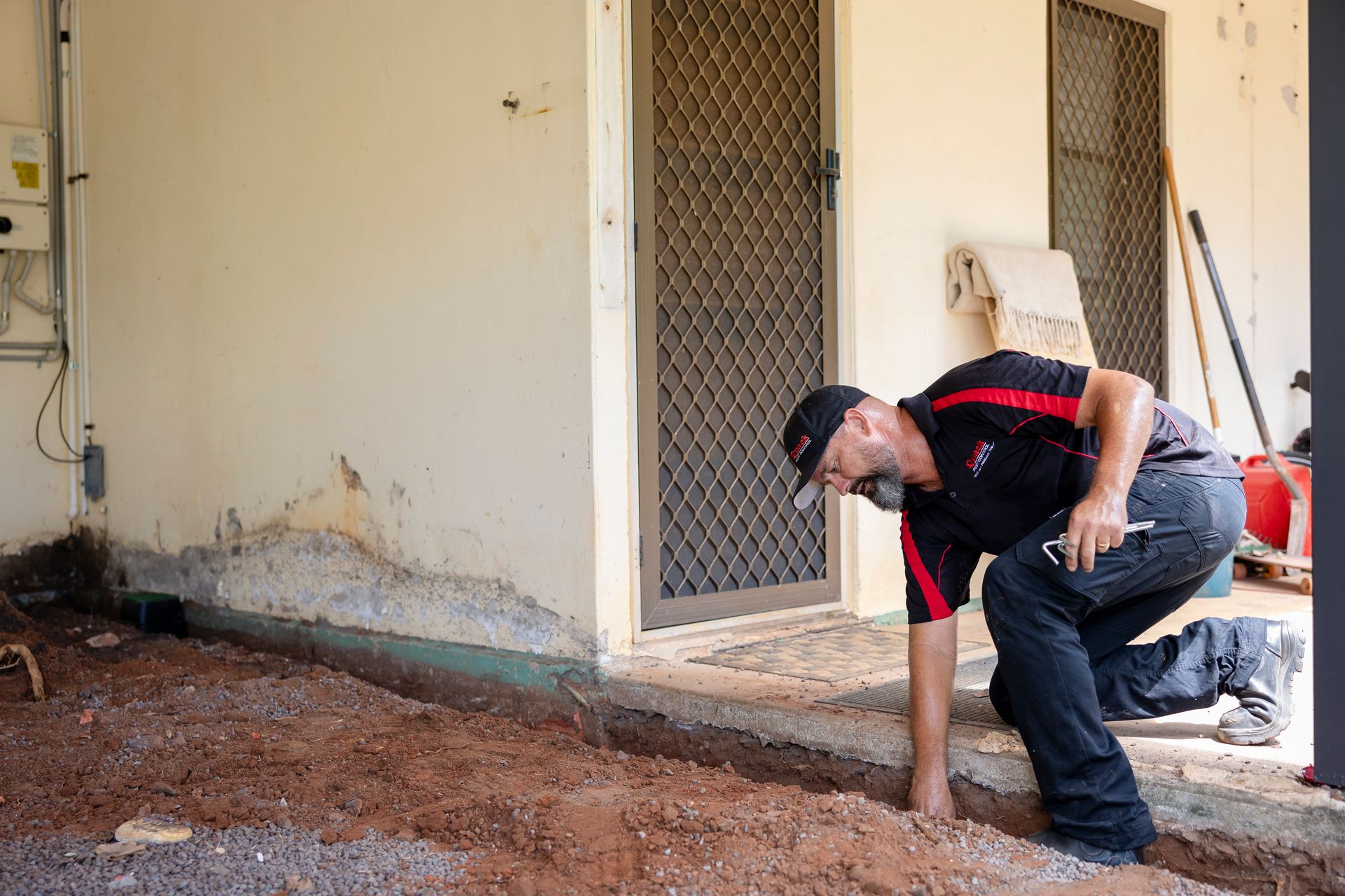 Man in Work Attire Inspecting Foundation Near a Door and Wall — Quack Pest Control in Berrimah, NT