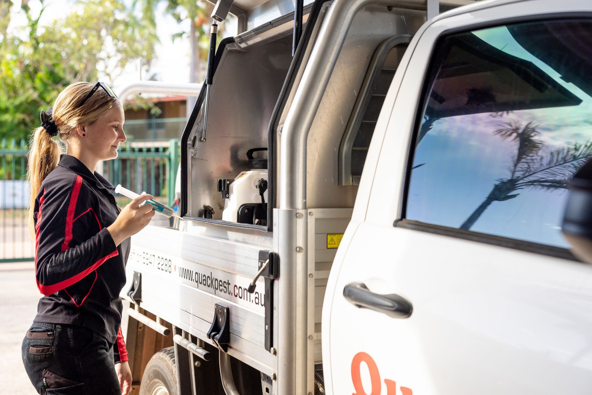 Woman in Uniform Holding Syringe Near a White Utility Truck Outdoors — Quack Pest Control in Fannie Bay, NT