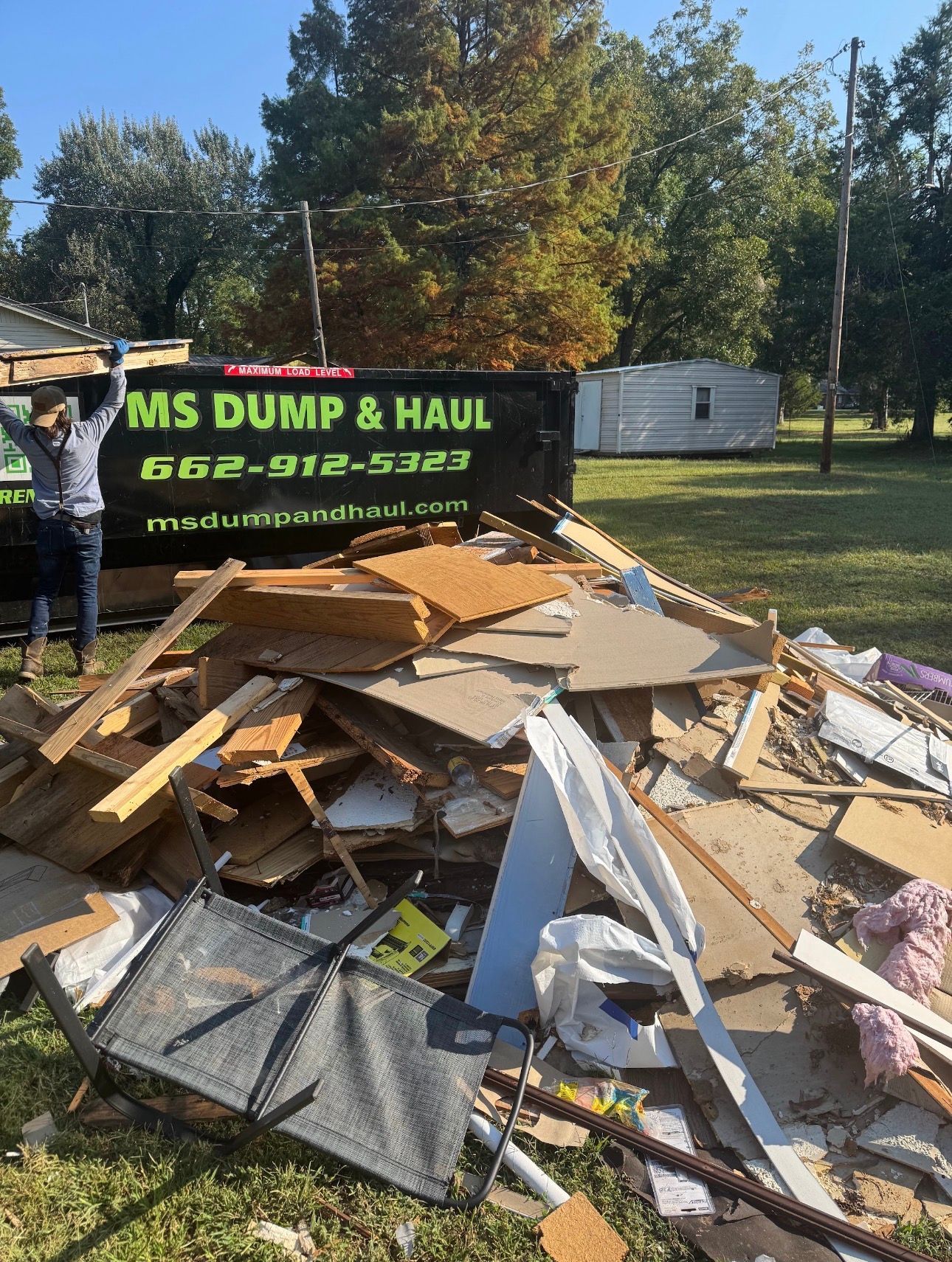 A person loading construction debris into a dumpster labeled 