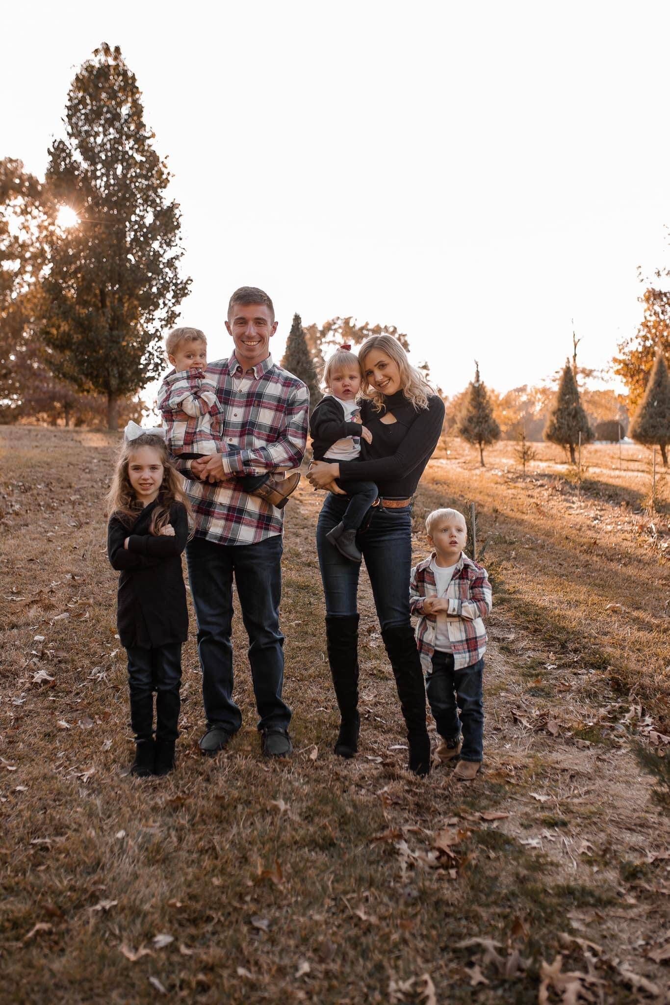 A family is posing for a picture at a christmas tree farm.