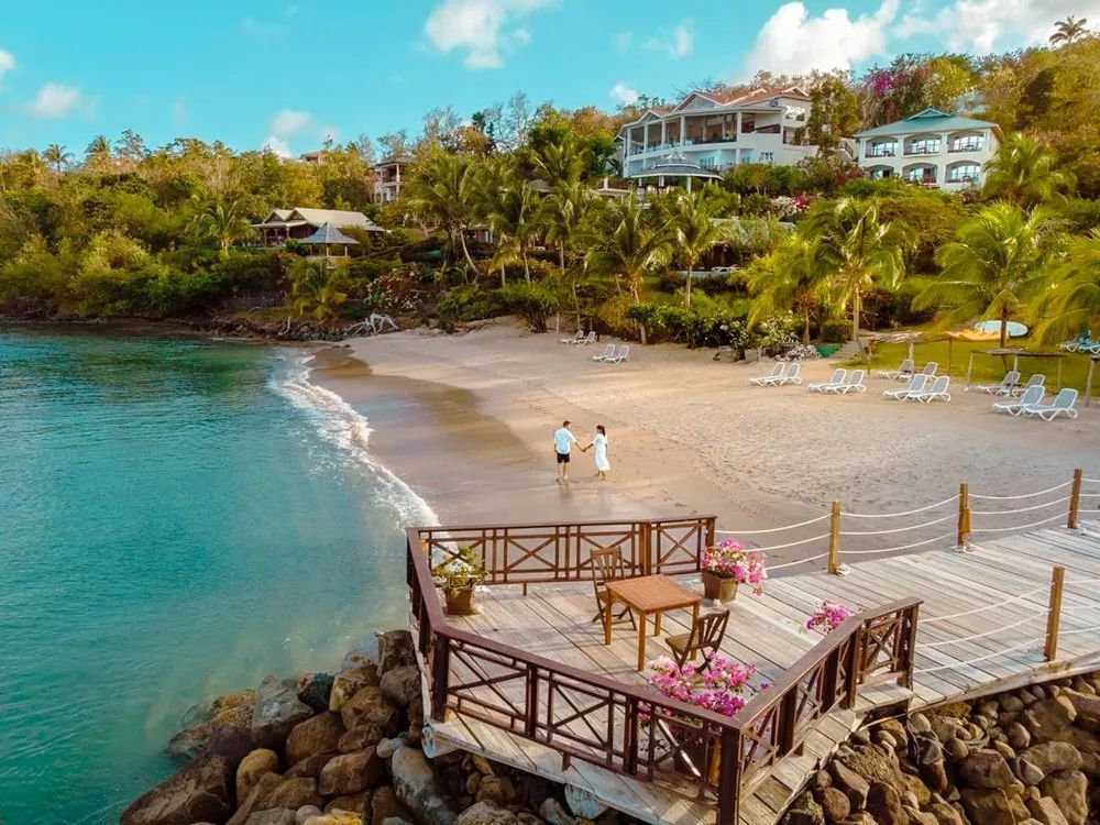 A couple is walking on a beach next to a dock.