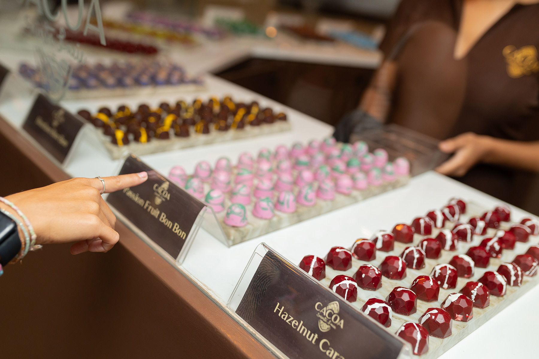 A person is pointing at a display of chocolates in a store.