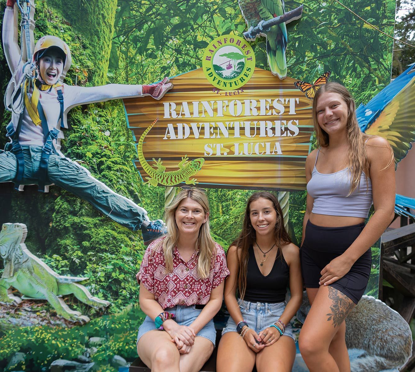 Three women are posing for a picture in front of a sign that says rainforest adventures