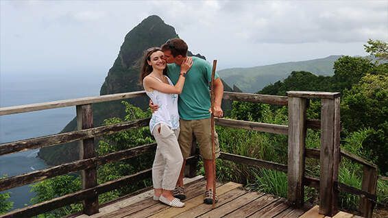 A man and a woman are kissing on a balcony overlooking the ocean.