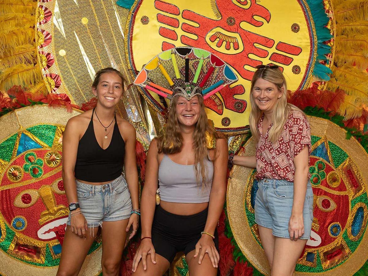 Three women are posing for a picture in front of a colorful costume.
