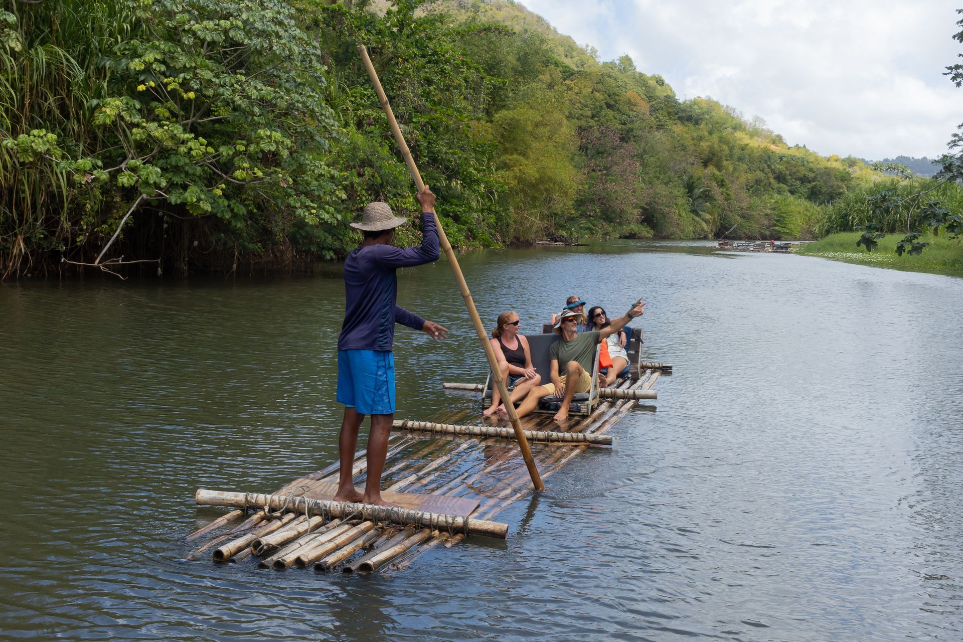 A man is rowing a raft with people on it in a river.