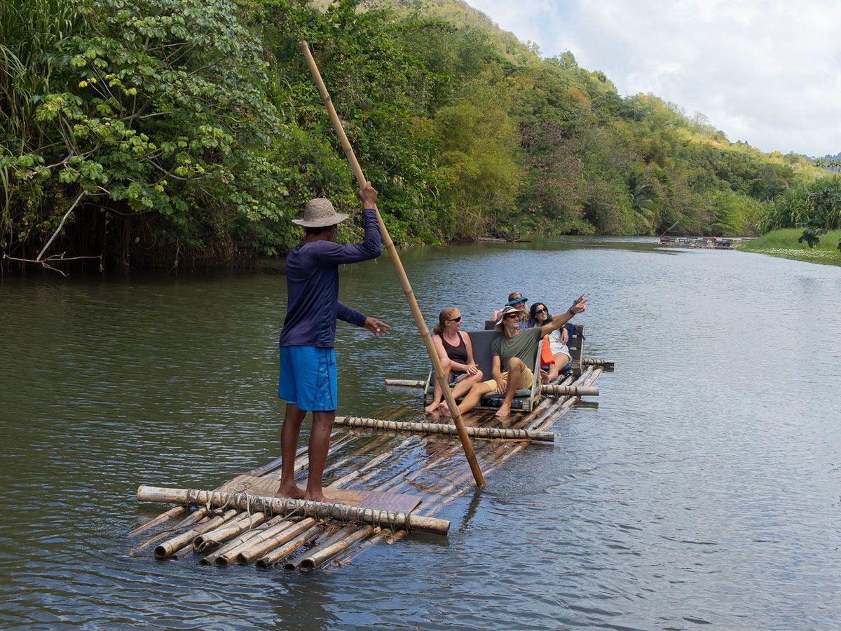 A man is steering a group of people on a bamboo raft.