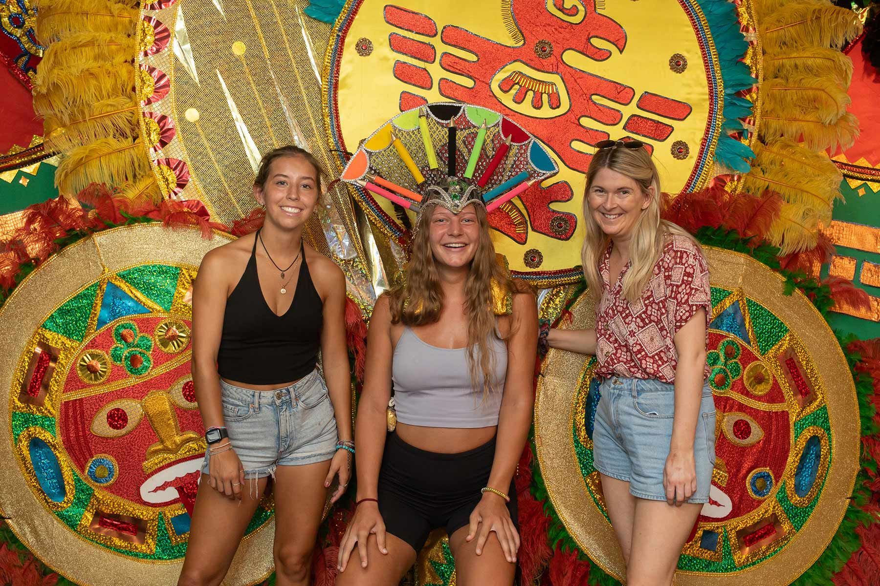 Three women are posing for a picture in front of a colorful costume.
