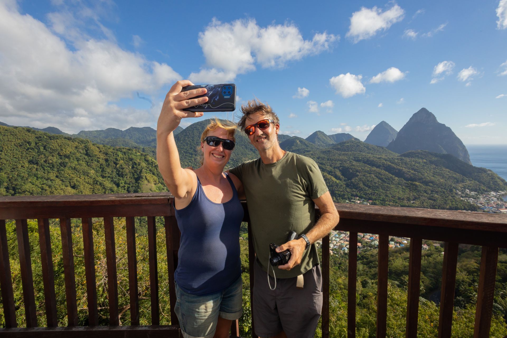 A man and a woman are taking a selfie on a balcony overlooking a mountain range.