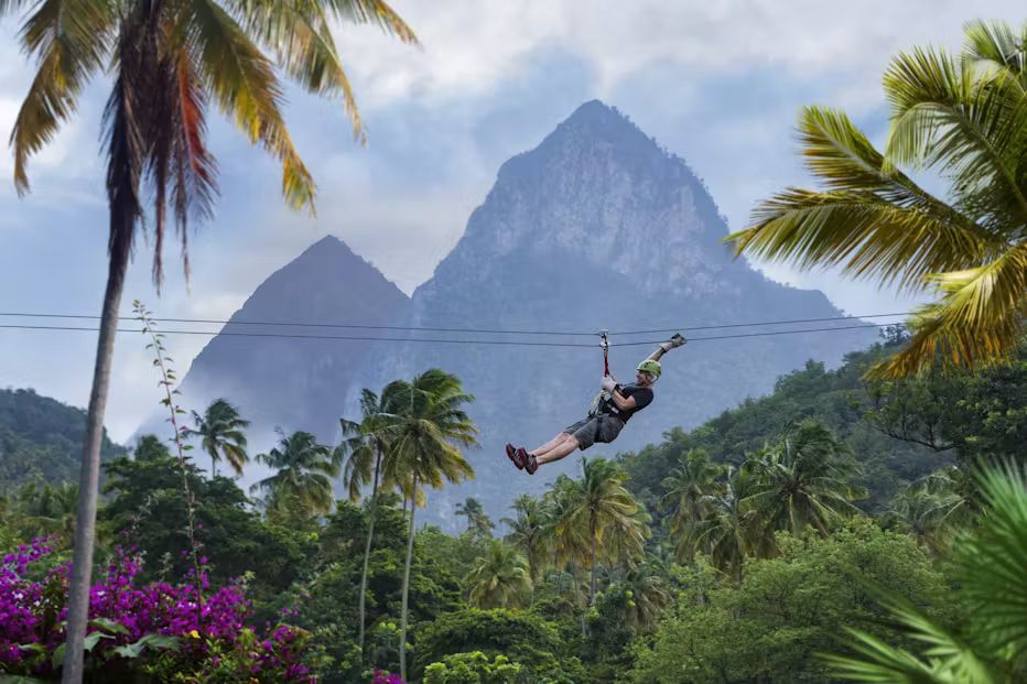 A man is flying through the air on a zip line with mountains in the background