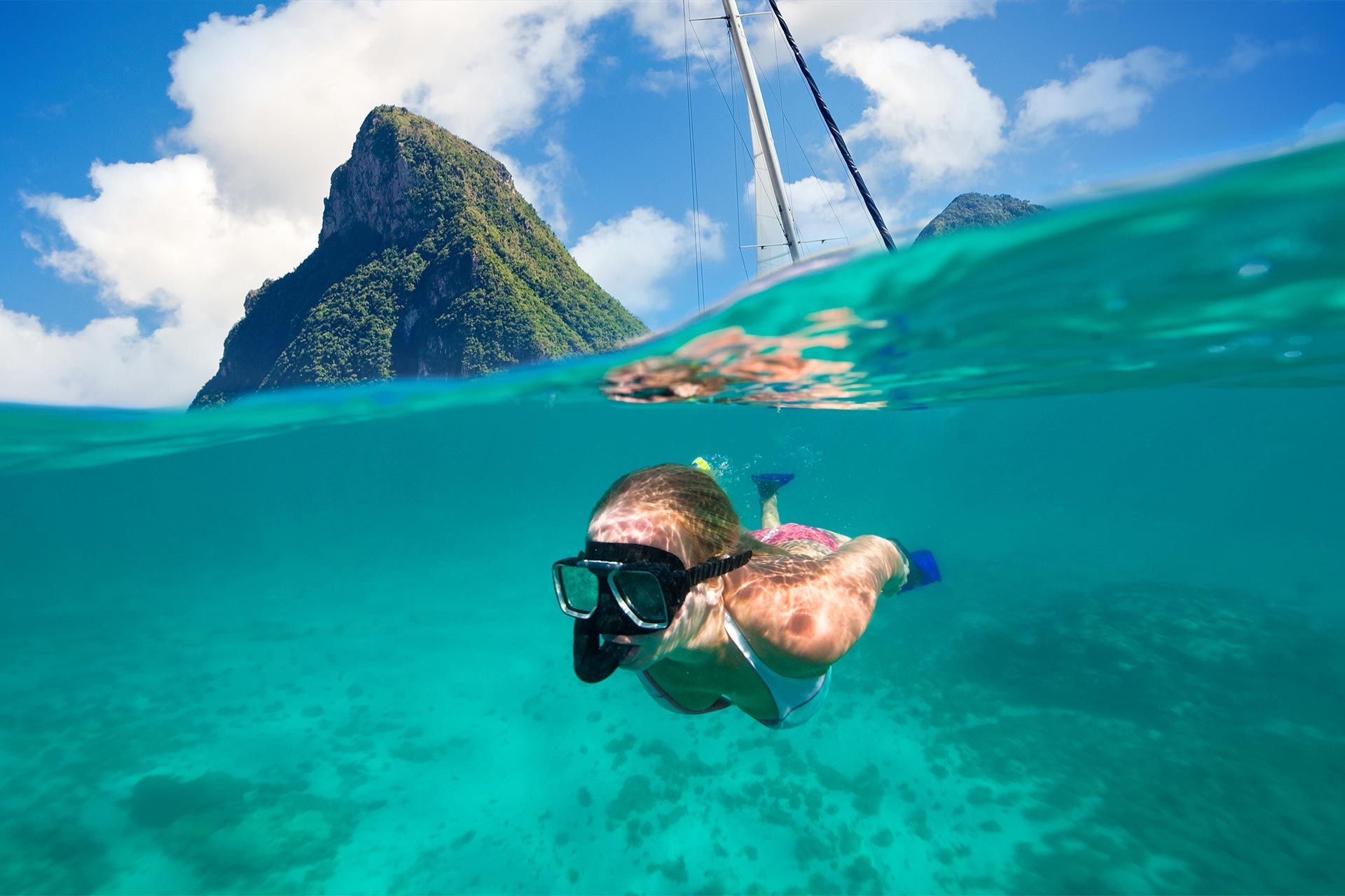 A woman is swimming in the ocean with a mountain in the background.