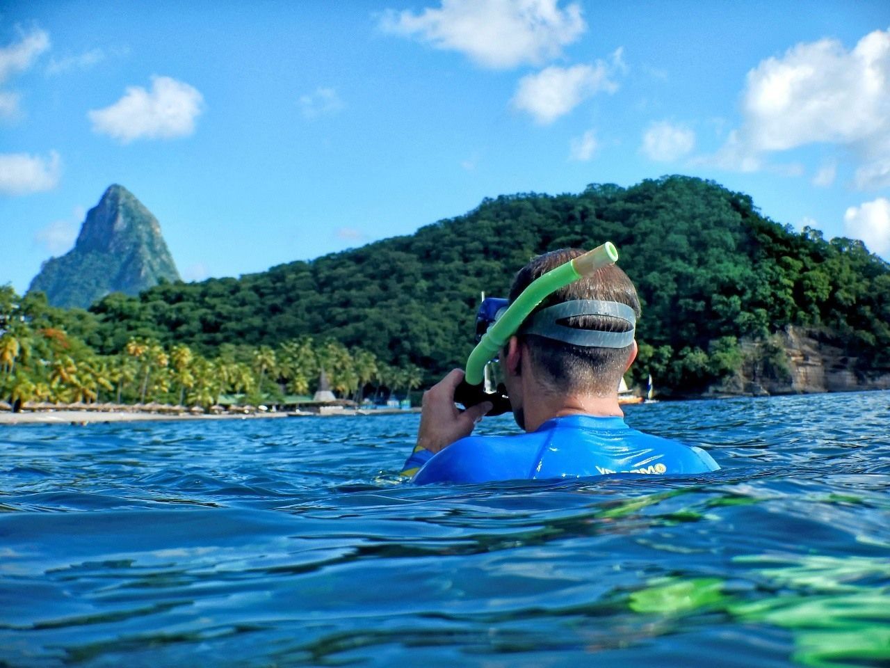 A man is swimming in the ocean with a mountain in the background.