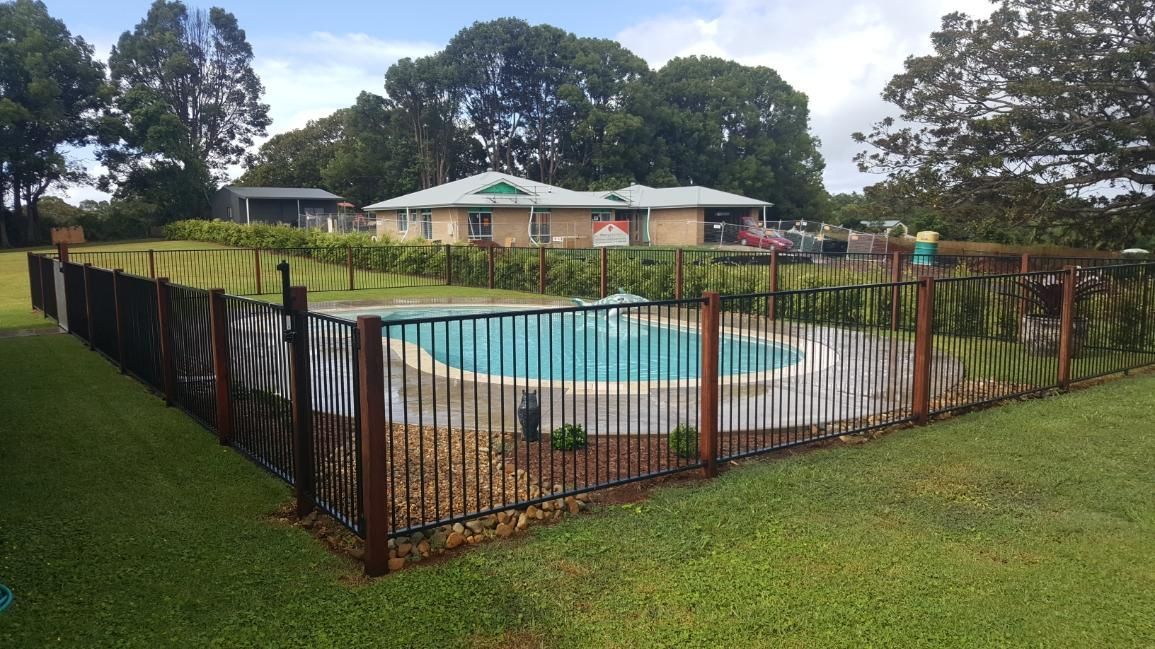 A fenced-in pool with a house in the background, set on a grassy lawn under a cloudy sky.