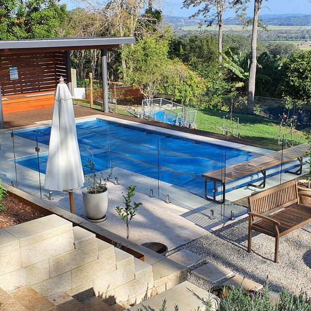 Backyard Pool with A Blue Cover, Wooden Benches, and Lush Greenery — Byron & Beyond Fencing in Billinudgel, NSW