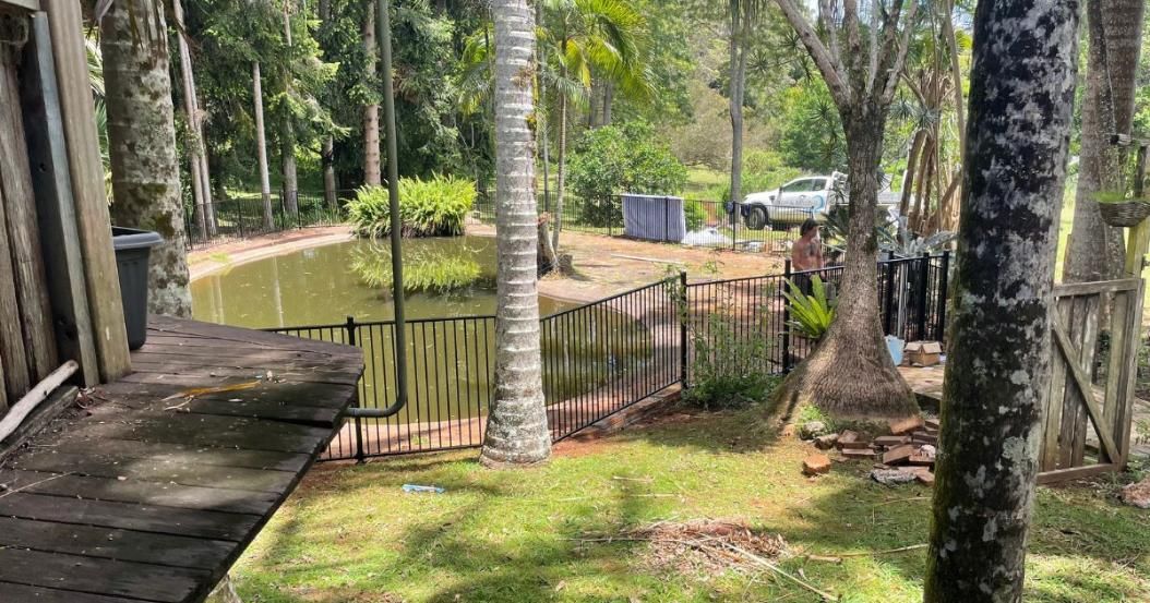 A Wooden Bench Is Sitting in The Middle of A Lush Green Field Next to A Pond — Byron & Beyond Fencing In Billinudgel, NSW